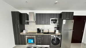 Eine moderne Küche mit dunklen Schränken, einer Mikrowelle, einem Kühlschrank, einer Waschmaschine und einer Kaffeemaschine.