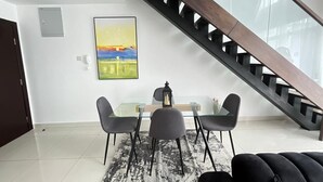 Ein moderner Essbereich mit einem Glastisch und Stühlen, einem schwarz-weißen Teppich und einem Sonnenuntergangsgemälde an der Wand.