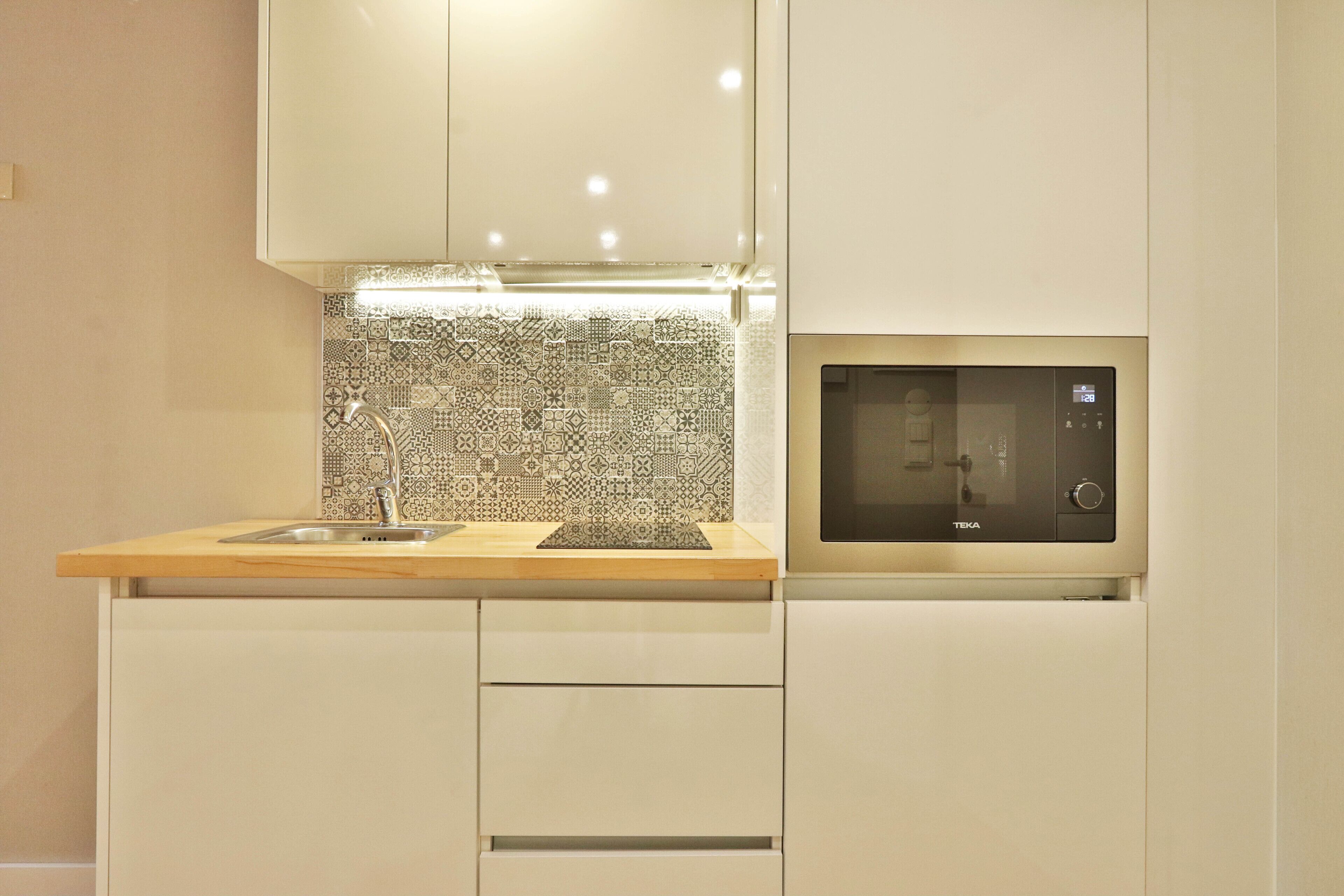 A modern kitchen with a microwave, sink, and patterned backsplash.