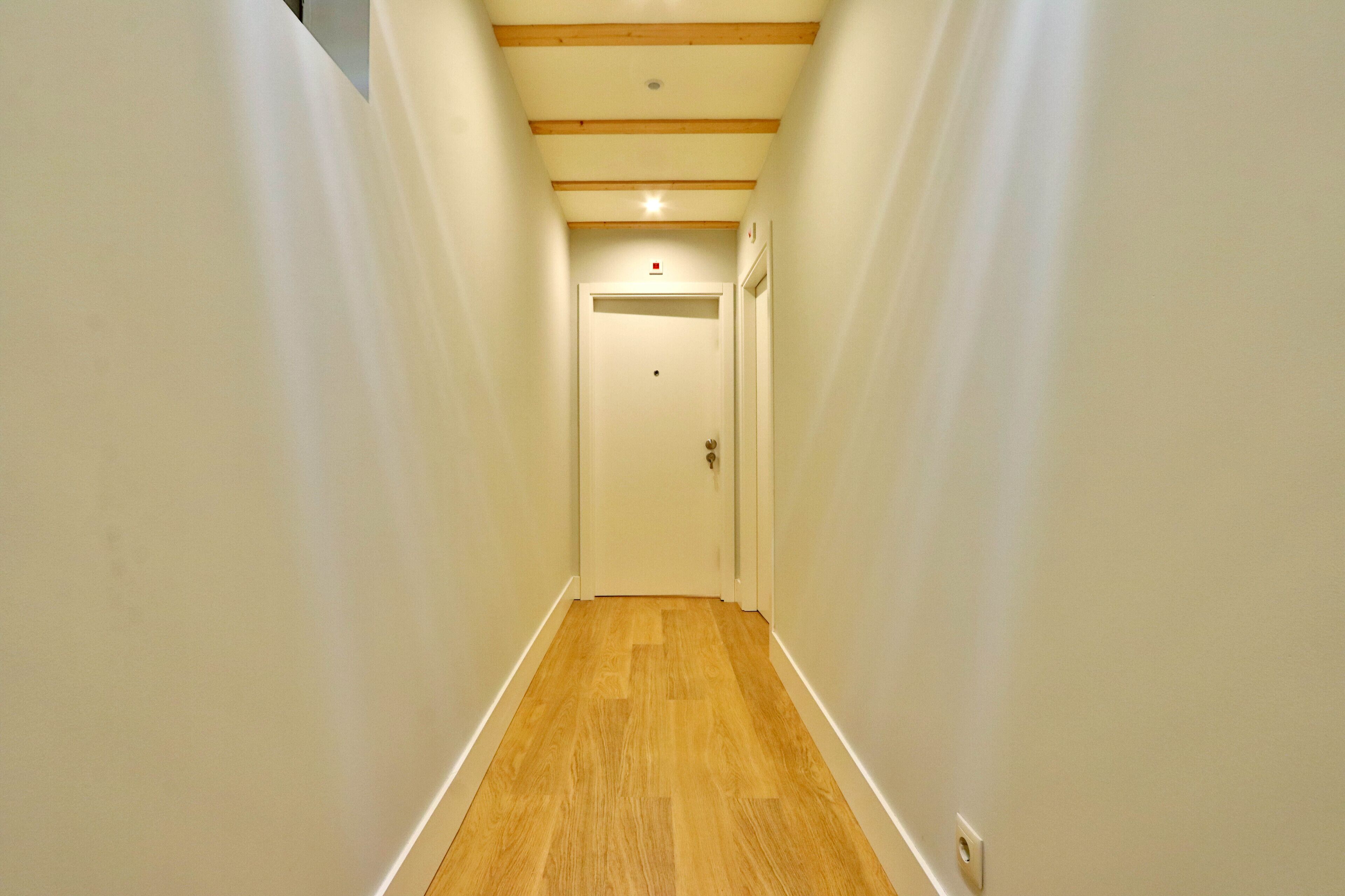 Un couloir étroit avec un plancher en bois et des murs blancs.