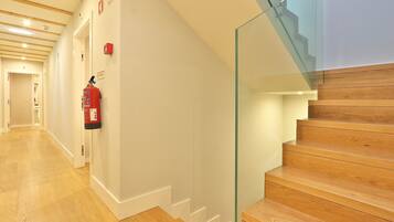 A hallway with wooden flooring, a fire extinguisher mounted on the wall, and a glass railing on a staircase.