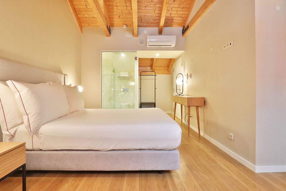 A modern bedroom with a large bed, wooden floor, and a ceiling with exposed beams.