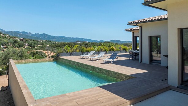 A swimming pool with a wooden deck, lounge chairs, and a view of mountains. - Villa A Trinita: Private paradise, infinity pool, gym and games room (Porto-Vecchio)
