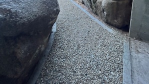 A pathway flanked by large rocks, leading to a building with a sloped roof. - Villa A Trinita: Private paradise, infinity pool, gym and games room (Porto-Vecchio)