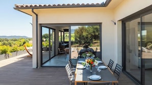 An outdoor dining area with a table set for four, surrounded by large sliding glass doors leading to a patio. - Villa A Trinita: Private paradise, infinity pool, gym and games room (Porto-Vecchio)
