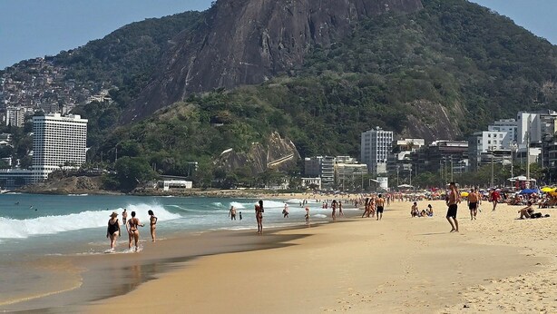 A beach with a prominent mountain in the background, sandy shore, and buildings along the coastline. - chale leblon (Rio de Janeiro)