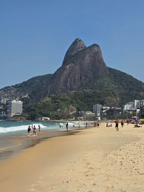 A beach with a prominent mountain in the background, sandy shore, and buildings along the coastline. - chale leblon (Rio de Janeiro)