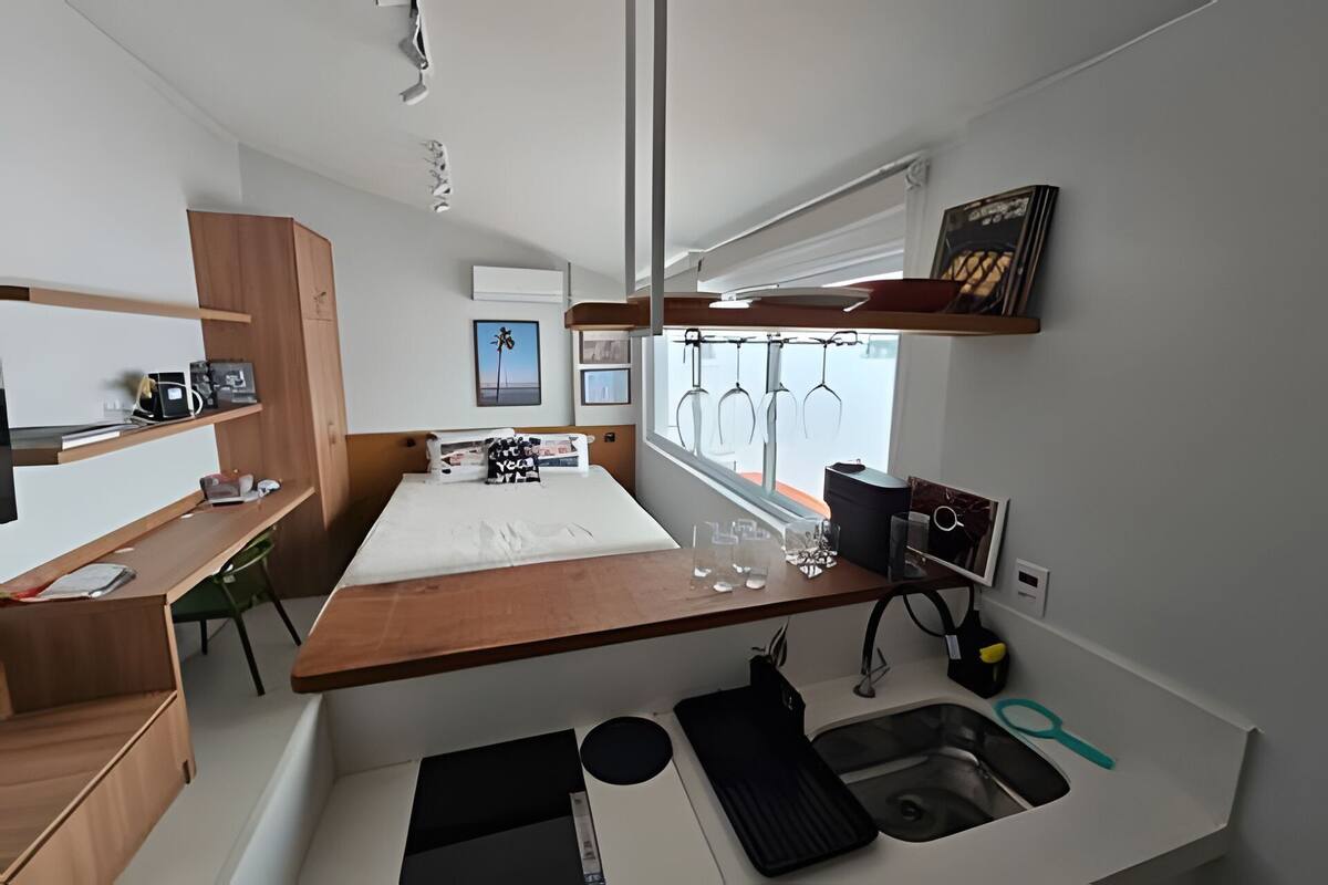 A compact, modern room with a bed, a small desk, a window with curtains, and a view of the sea.