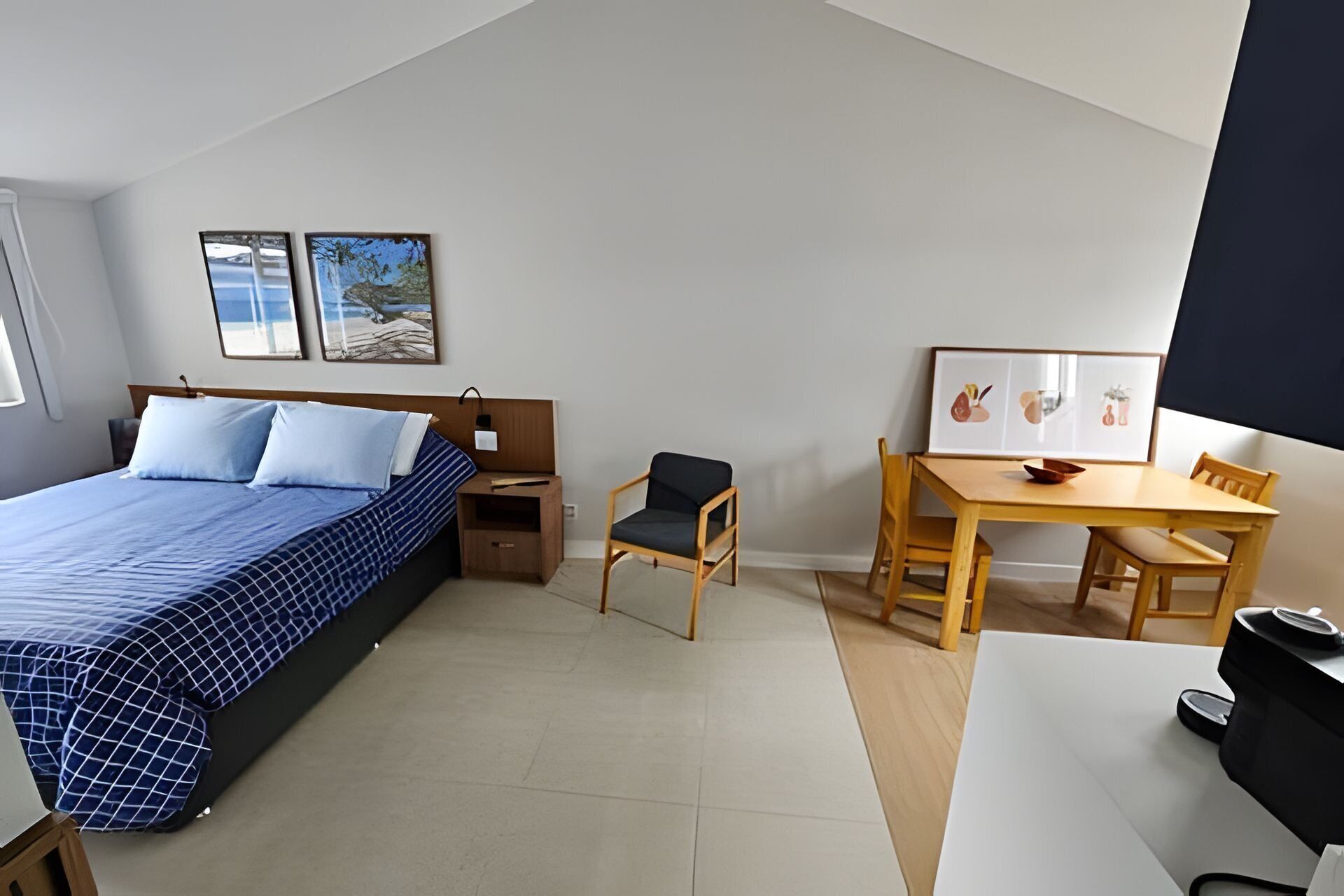 A bedroom with a bed, a desk, and a chair. There are two framed pictures on the wall.