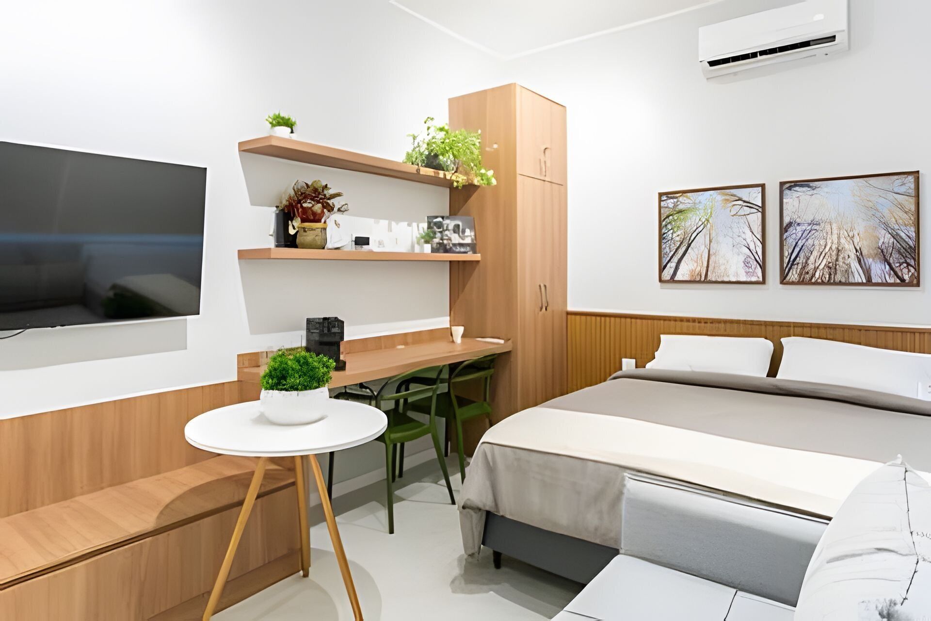 A modern hotel room with a bed, a desk, a TV, and two wall-mounted paintings.