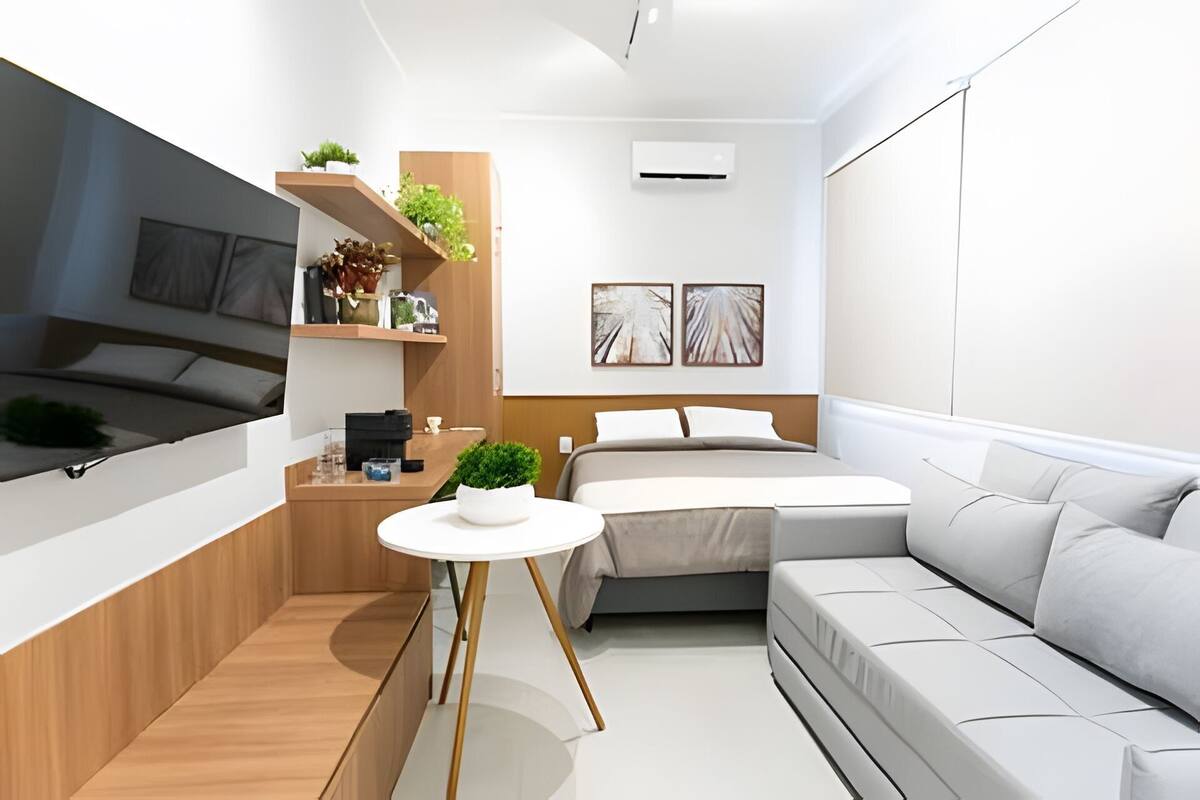 A modern, compact bedroom with a bed, a sofa, a small table, and shelves with plants.