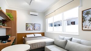 A modern hotel room with a bed, a sofa, a small table, and a window with a view of a building. - chale leblon (Rio de Janeiro)
