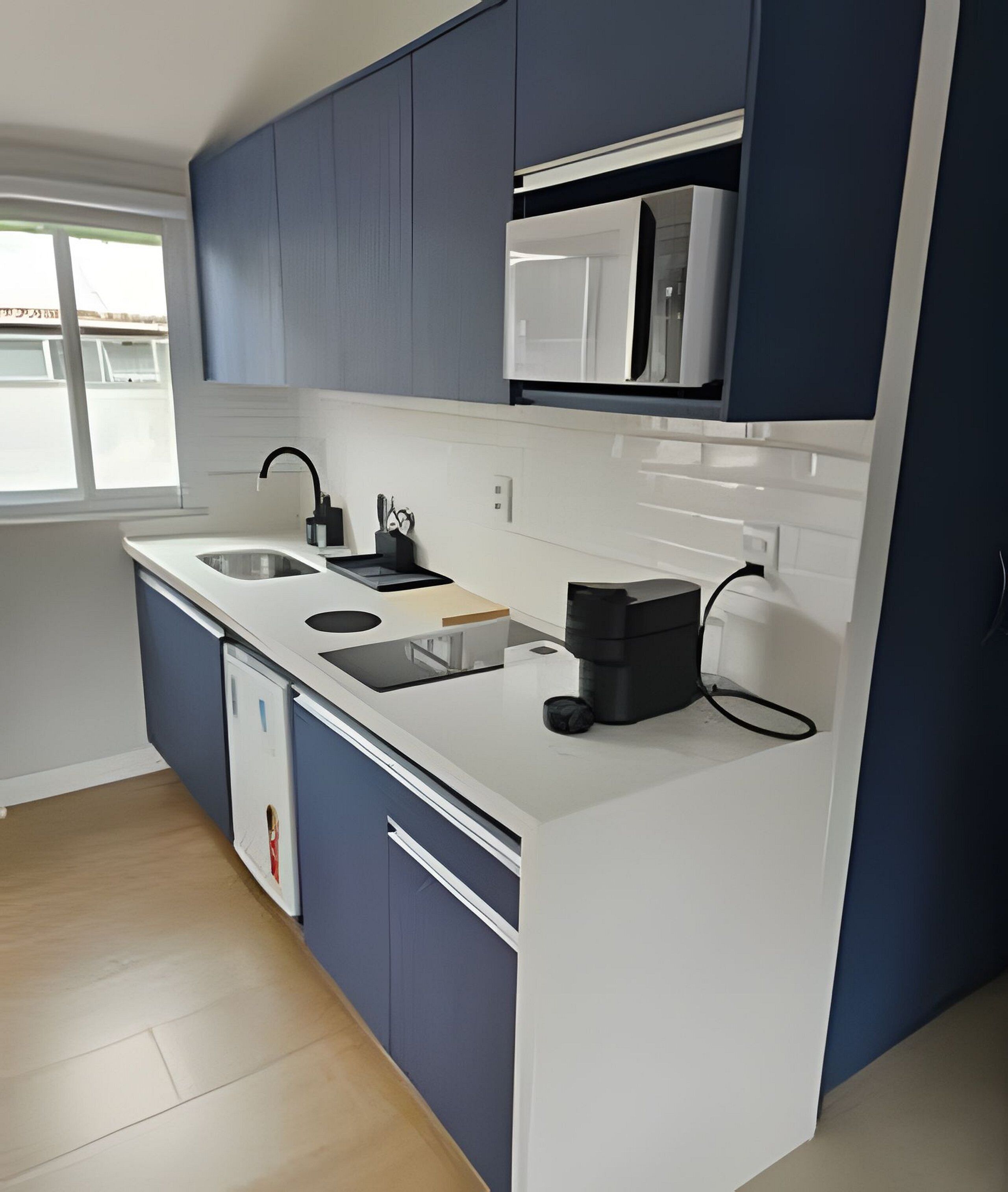 Une cuisine moderne avec des meubles de couleur bleu foncé, un plan de travail blanc, un four à micro-ondes encastré et une machine à café.