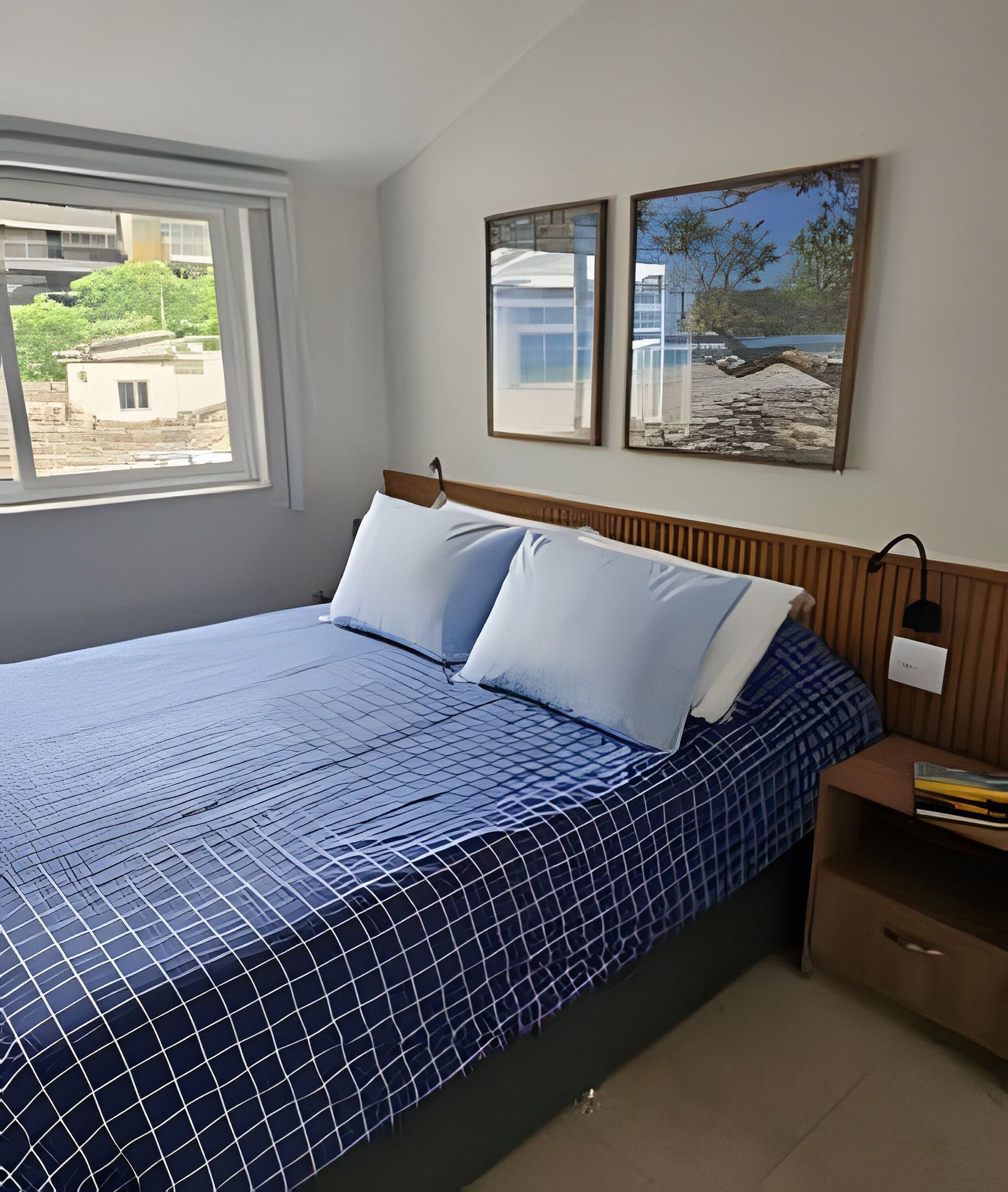 A bedroom with a bed, a nightstand, a window, and two framed pictures on the wall.