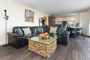 A modern living room with a glass coffee table, a sofa, and a dining area with chairs.