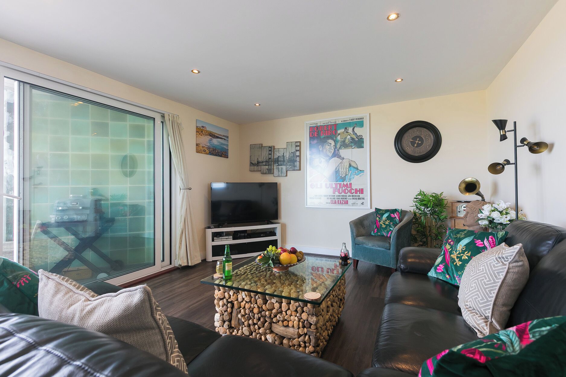 A living room with a sofa, a glass coffee table, a television, and a poster on the wall.
