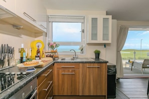 A modern kitchen with a large window, wooden cabinets, and a view of the sea.