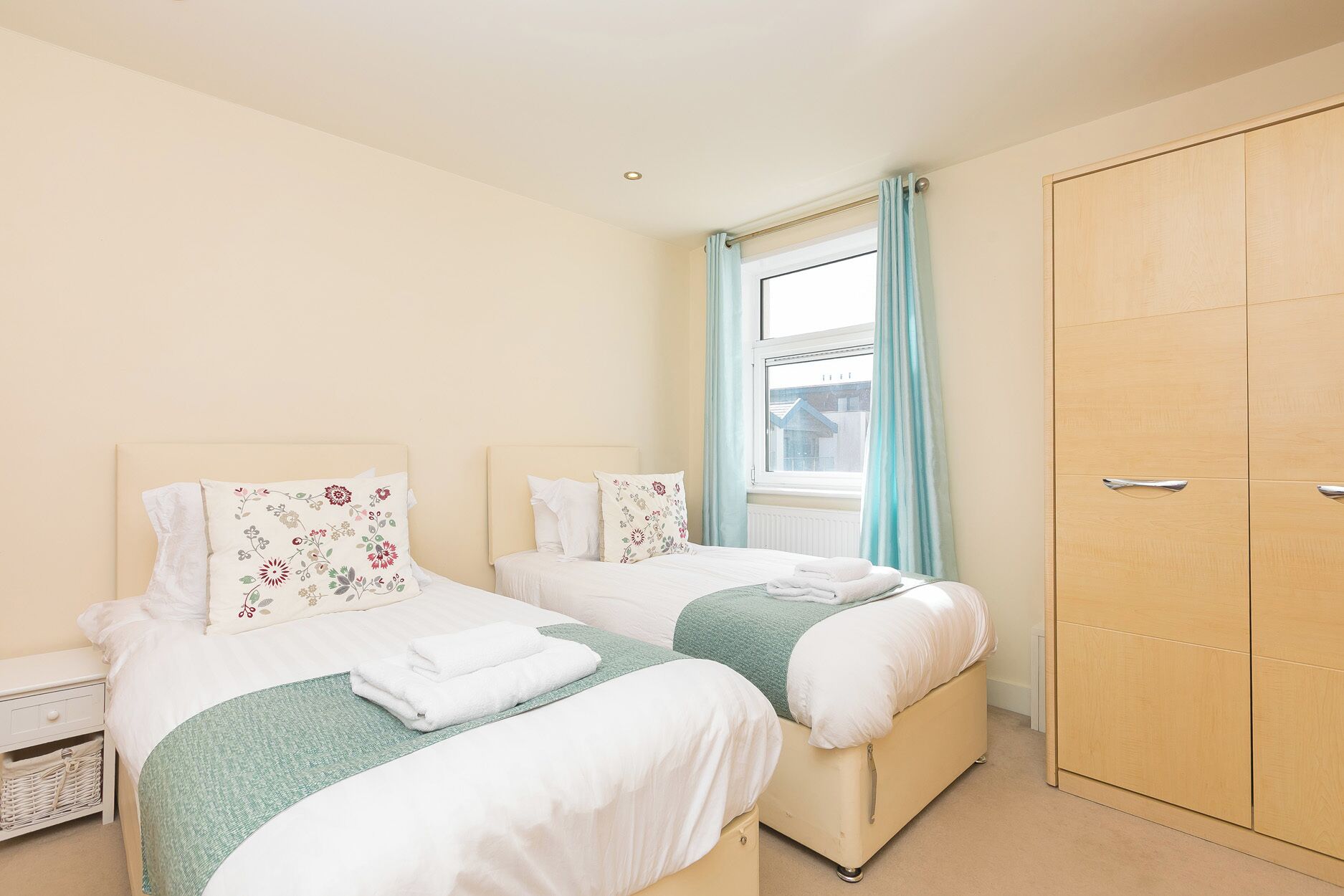 A bedroom with two beds, a wardrobe, and a window with curtains.