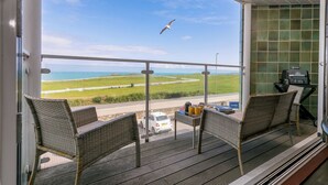 Ein Balkon mit Korbstühlen, einem Grill und Blick aufs Meer.