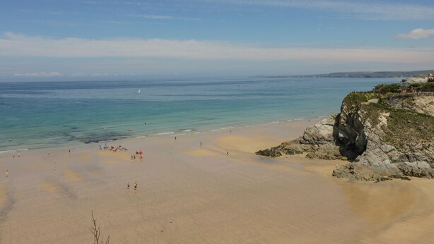 Ein Strand mit blauem Himmel, ruhigem Wasser und felsigen Klippen.