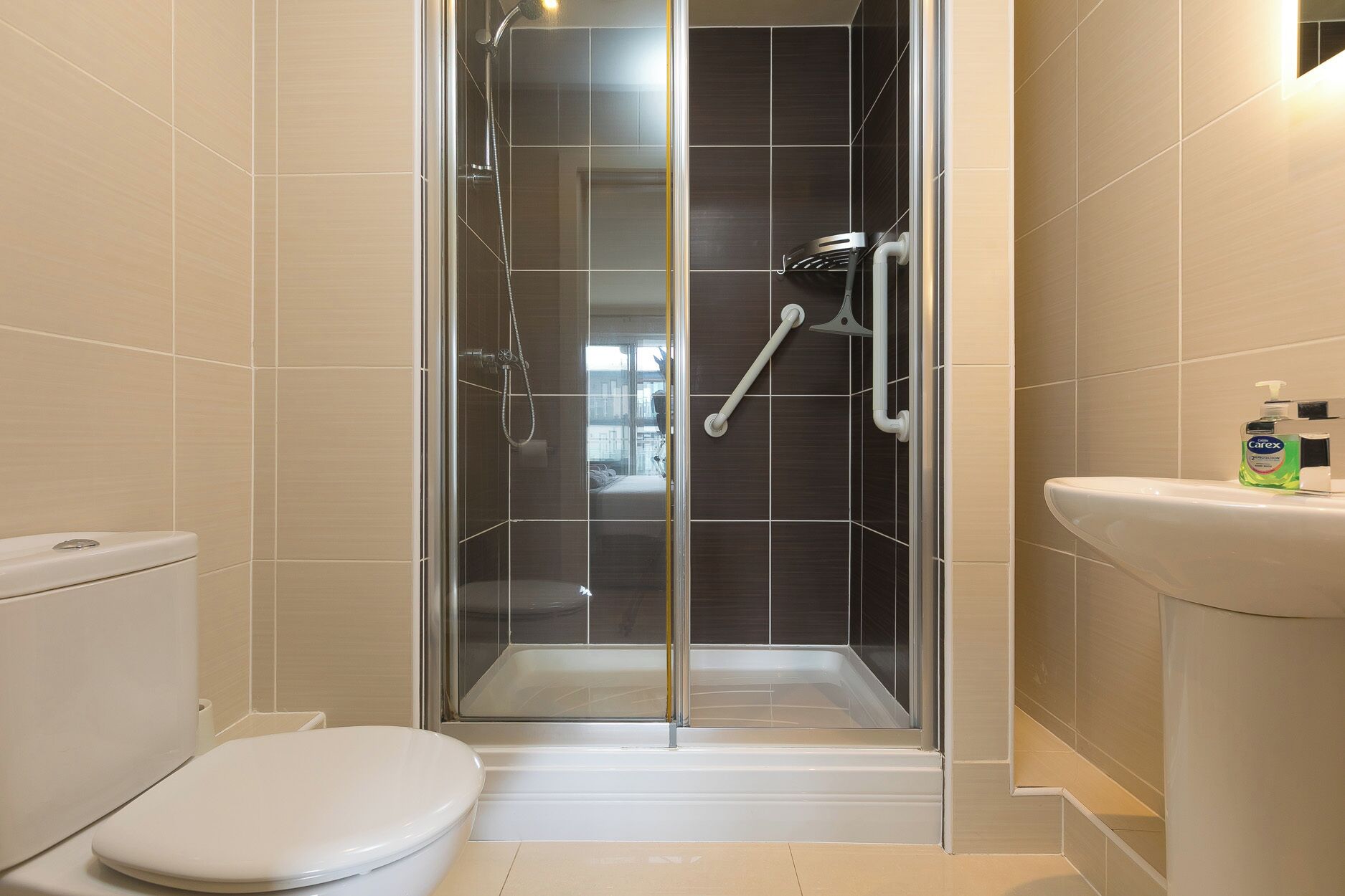 A modern bathroom with a glass-enclosed shower, a white toilet, and a sink with a bottle of hand soap.