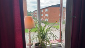 Una ventana con vista a un edificio de ladrillo y una planta en una maceta blanca.