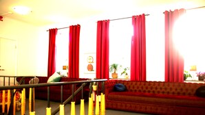 Una sala de estar con un sofá rojo, una escalera con barandillas amarillas y vistas al exterior a través de ventanas grandes con cortinas rojas.