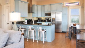 Une cuisine moderne avec des meubles bleus, un îlot central doté de tabourets, des appareils en acier inoxydable et un coin repas avec une table et des chaises.