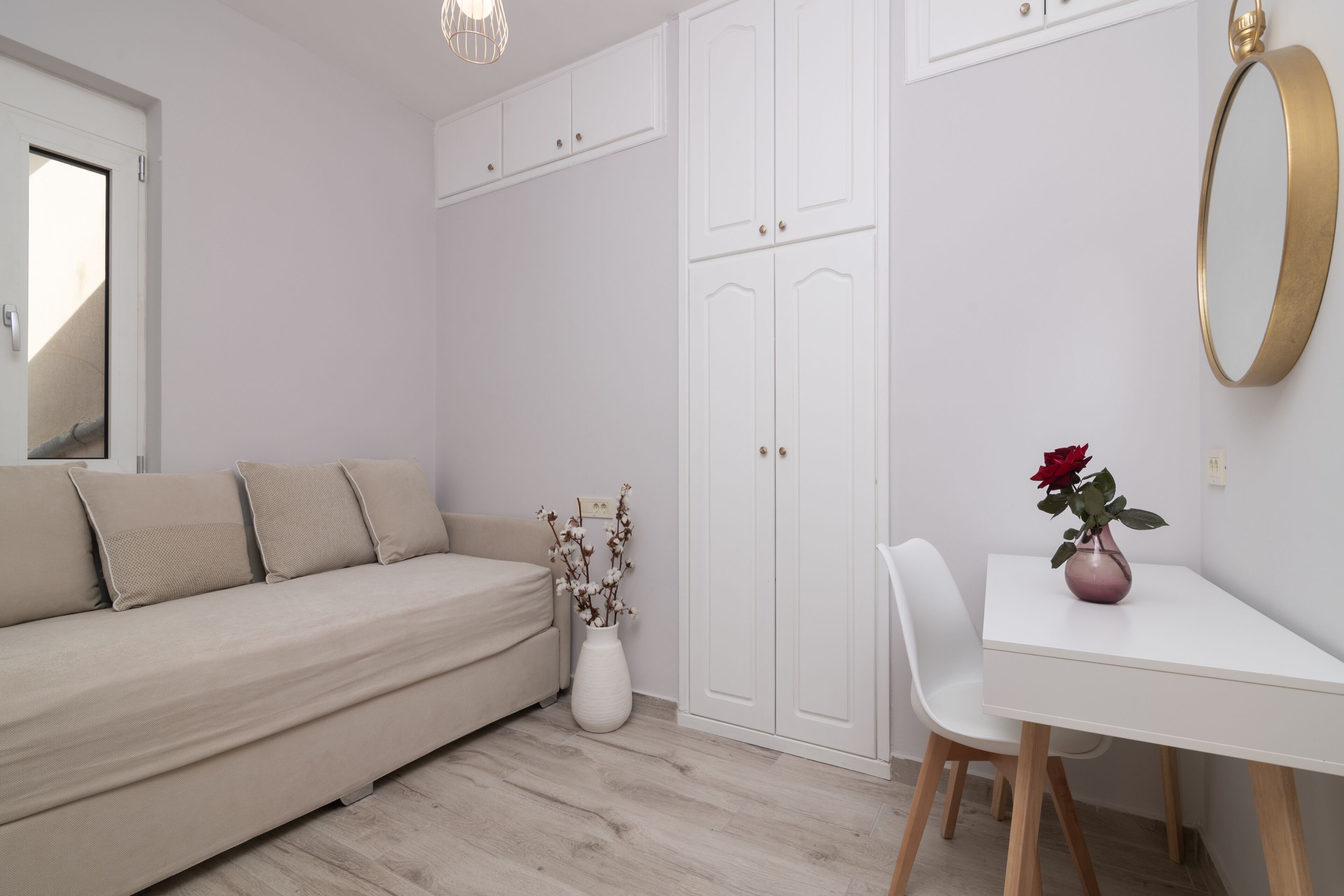 Ein schlicht eingerichteter Raum mit einem beigen Sofa, einem weißen Schreibtisch und einem weißen Kleiderschrank.