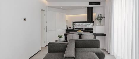 A modern living room with a grey sectional sofa, a flat-screen TV, and a kitchen area in the background.