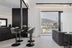 Una cocina moderna con dos taburetes de bar, una zona de comedor con mesa y sillas, y un ventanal con vistas a la ciudad y montañas.