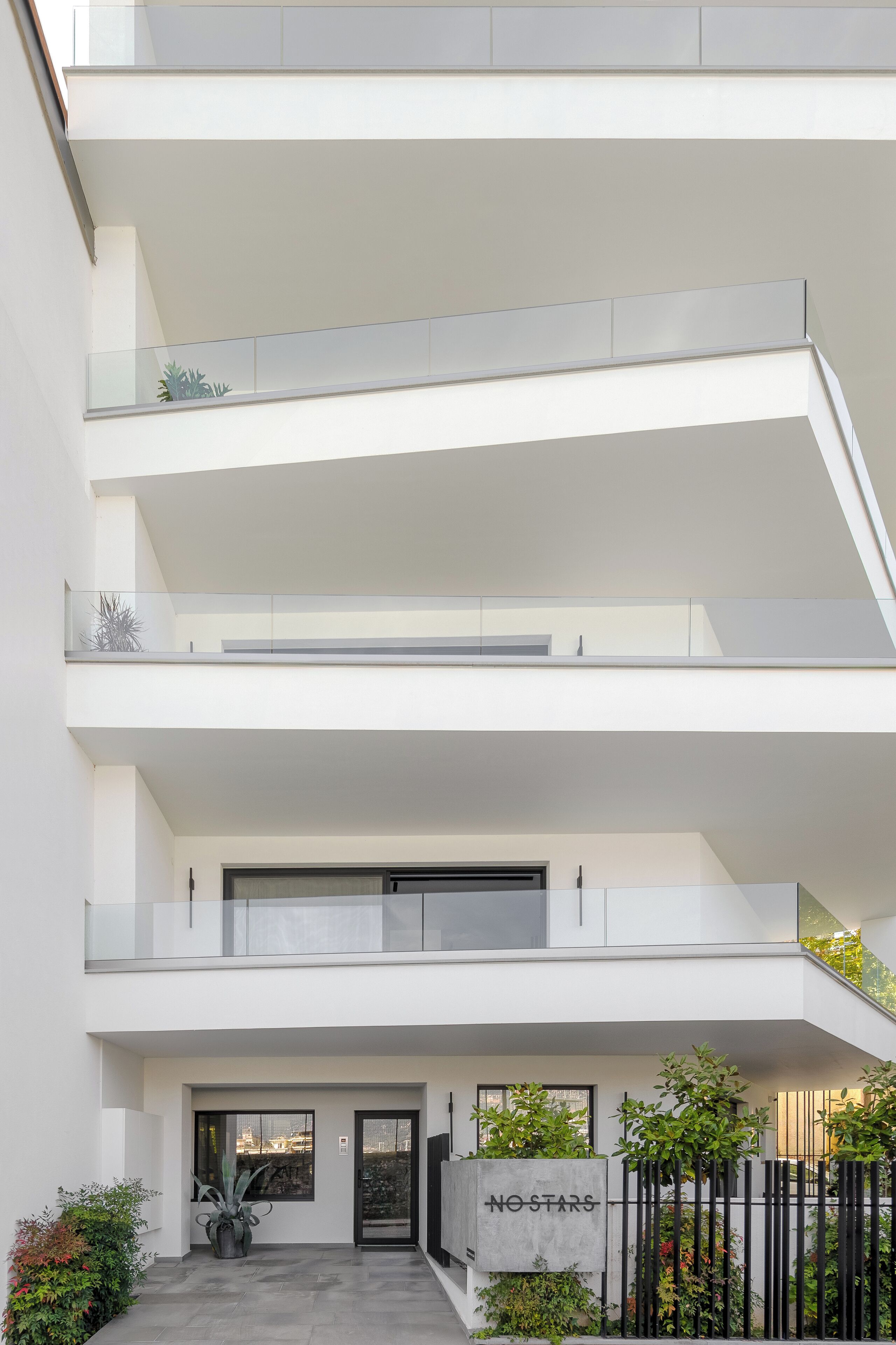 A multi-story residential building with a minimalist design, featuring balconies, a concrete entrance, and a sign that reads "NO STARS".