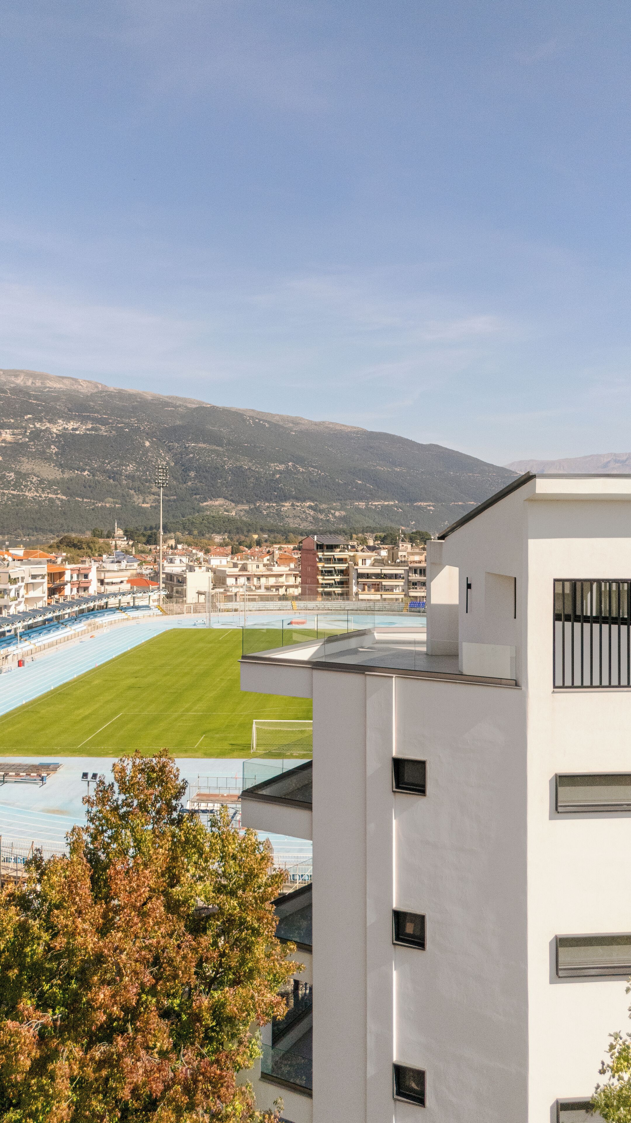 Blick auf ein Sportstadion mit einem grünen Spielfeld, Zuschauerbereichen und einer Bergkulisse.