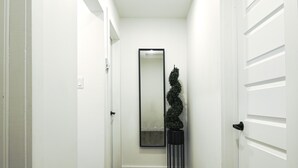 Un pasillo estrecho con paredes blancas, suelo de madera, una puerta negra y un espejo con marco negro en la pared.