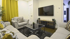Una sala de estar moderna con sofá, sillón, mesa de centro y televisor montado en la pared.