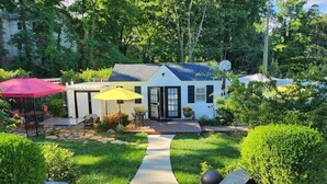 A small white house with a dark roof, a patio with outdoor furniture, and a pathway leading to the house. - Tiny House, Big Amenities – Home  (Asheville)