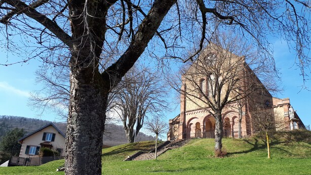 Une église dotée d’un grand clocher et un bâtiment dont le toit est en pente.