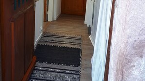 Un couloir avec une porte en bois, un tapis à motifs et un rideau blanc.