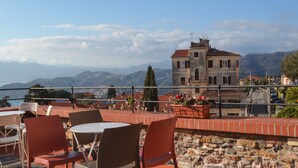 Une terrasse avec des sièges extérieurs, un mur en pierre et une vue sur une montagne et un bâtiment situé au loin.