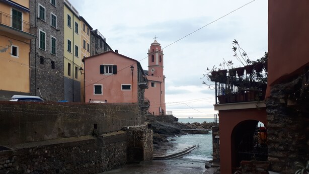 A narrow street with stone walls and buildings, including a pink building with a clock tower. - Demivie Guesthouse  (Lerici)