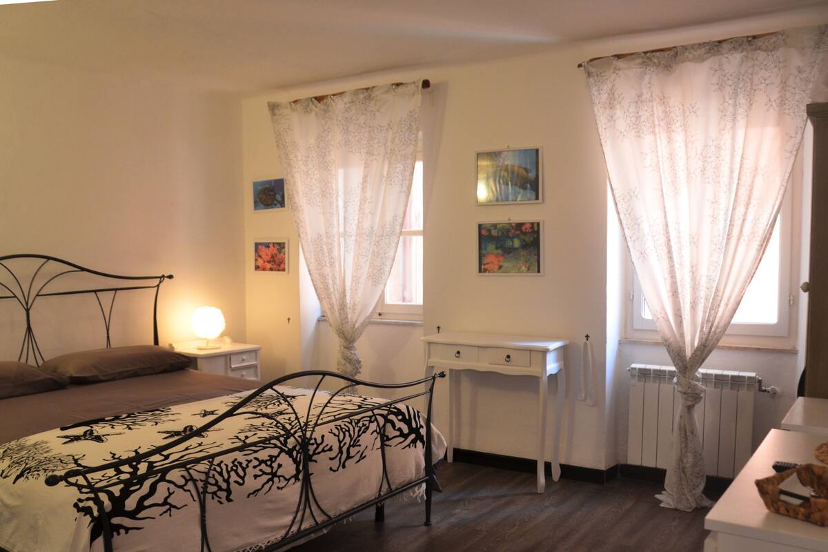 A bedroom with a bed, bedside tables, a desk, and curtains.
