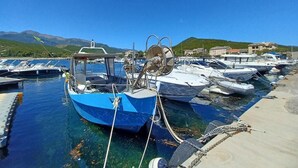 A marina with several boats docked, clear blue water, and a hilly landscape in the background.