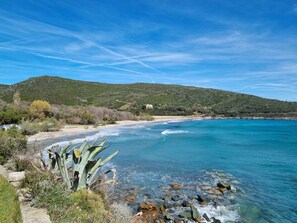 A coastal landscape with clear blue waters, rocky shore, and a hill with sparse vegetation. - Les Citronniers - View on the sea and the little harbor of Santa Severa (Luri)