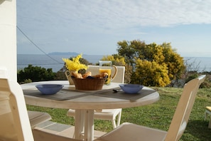 Una mesa al aire libre con vista al mar, una cesta de pan y un vaso de jugo.