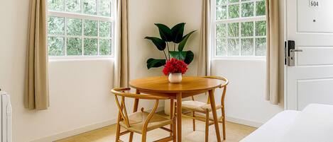 A hotel room with a round wooden table, two chairs, a potted plant, and a bed.