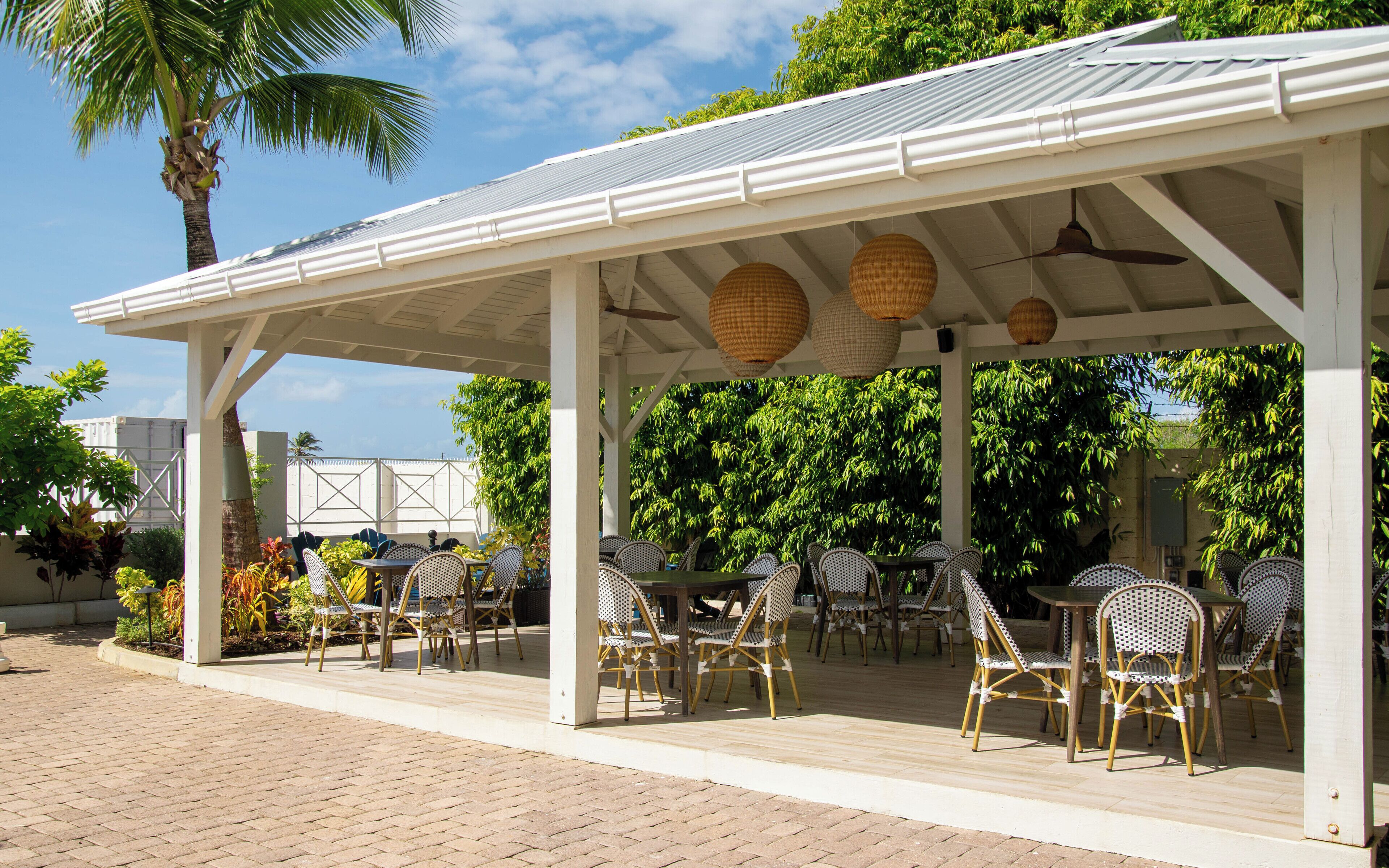 An outdoor patio with white metal roof, wicker chairs, and tables.
