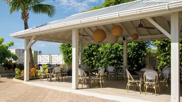 An outdoor patio with white metal roof, wicker chairs, and tables.