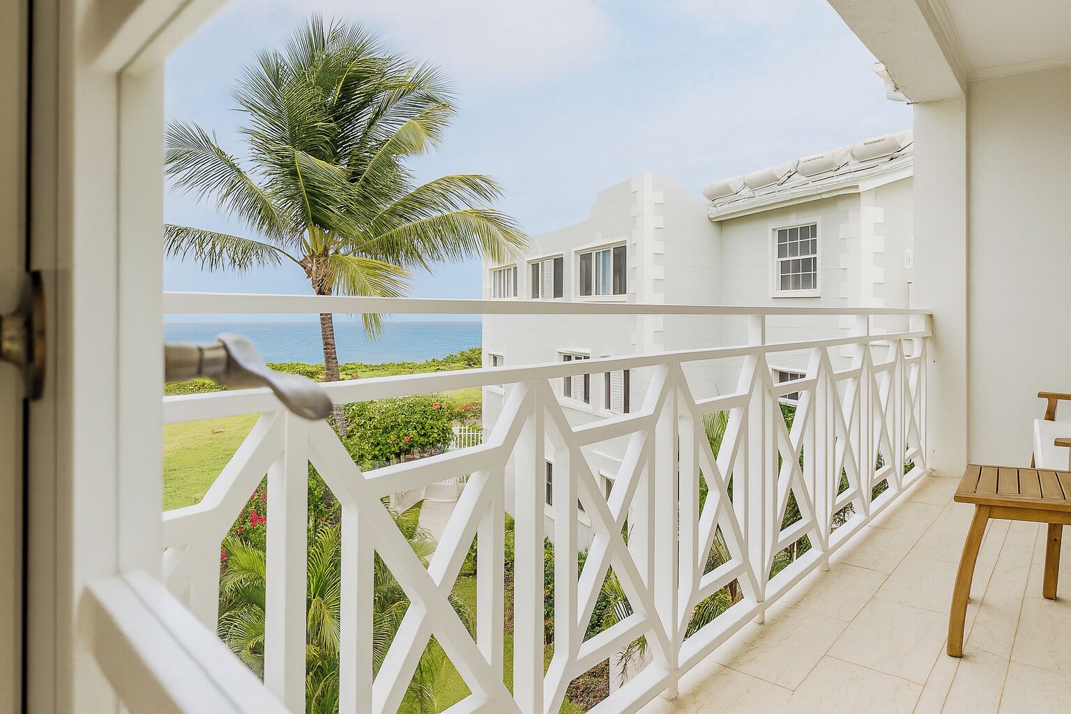 A balcony with a white railing, a wooden table, and a view of a white building and palm tree.