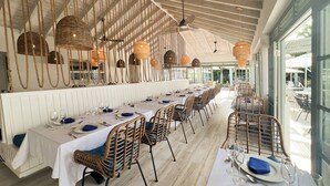 Un restaurante con mesas largas, sillas de mimbre y lámparas colgantes.