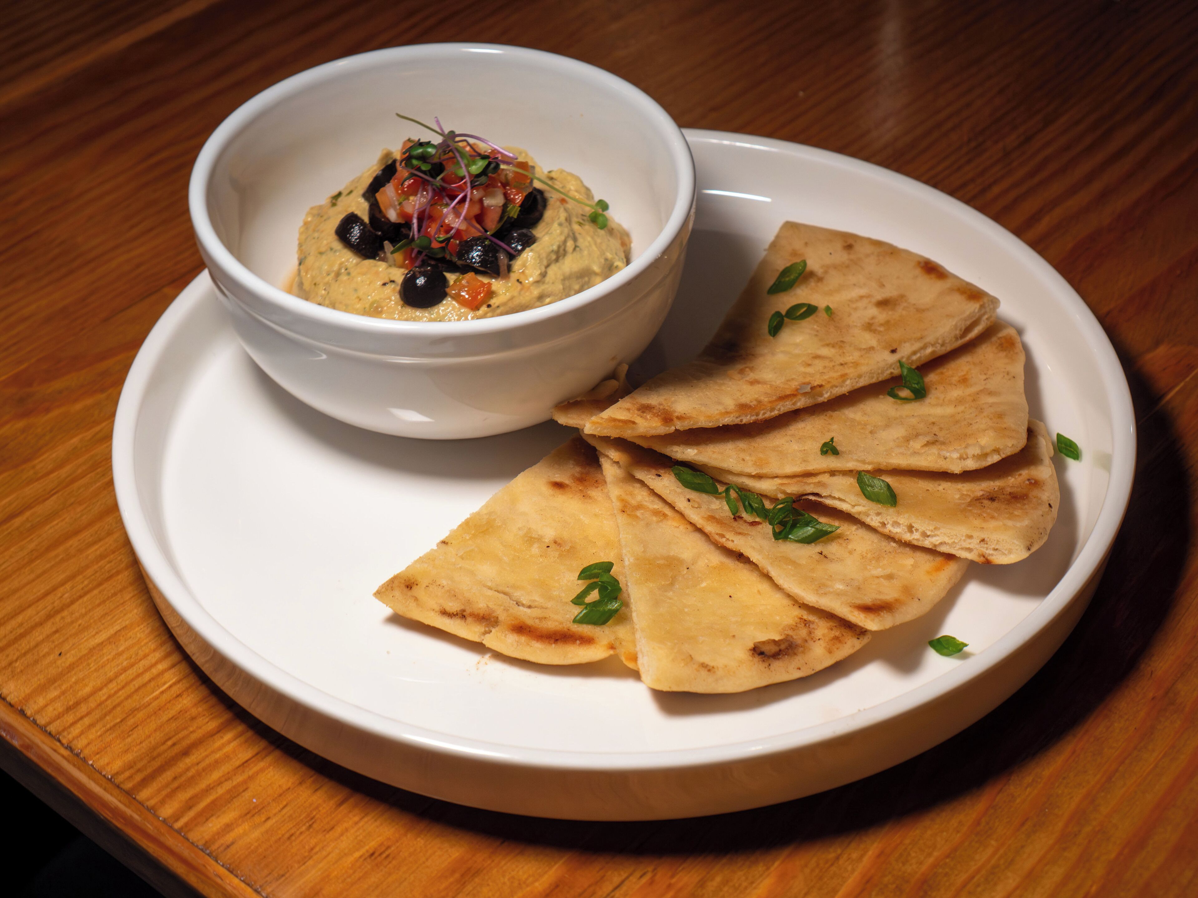Une assiette avec un bol de houmous et du pain pita.
